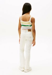 Weißes gestricktes Cropped-Top mit bunten Rautenmustern; kombiniert mit weißen Jeans. Auffällige Details umfassen ein Markenlabel am Taillenbund.