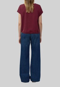 Korte mouwen, bordeaux blouse gecombineerd met wijde, hoog-gebroken blauwe spijkerbroek. De spijkerbroek heeft achterzakken en een klassieke denimtextuur.