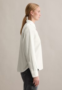 Witte, lange mouwen overhemd met knopen en kraag, recht gesneden, geweven stof en een klein geknoopte manchetdetail. Draagt het over donkere jeans.