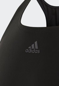 Reggiseno sportivo nero dal design elegante, realizzato in tessuto liscio. Caratterizzato da un colletto rotondo, stile racerback e un discreto logo Adidas in rilievo.