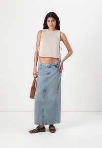 Un crop top tricot beige clair avec des liens sur les côtés, associé à une longue jupe en denim bleu clair. Des ballerines à motifs léopard noir et marron et un sac à main marron.