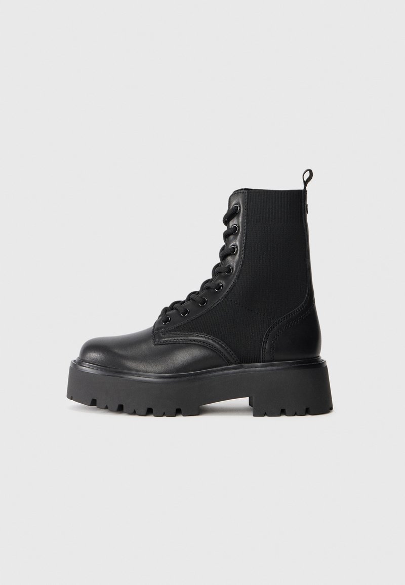 Black lace-up leather boot with thick rubber sole and knitted stretchy ankle panel, side view on plain light background.