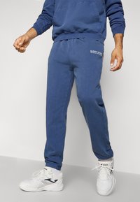 Μπλε φόρμες από ύφασμα βαμβακερού μείγματος, που διαθέτουν ελαστική μέση και μανσέτες, με λογότυπο εκτυπωμένο στο αριστερό ισχίο.