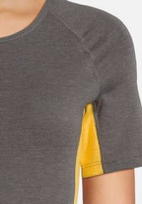 Maglietta sportiva grigia con maniche corte e pannelli laterali in rete gialla. Tessuto morbido e testurizzato con cuciture piatte per il massimo comfort.
