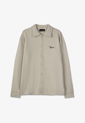 Bež košulja od vaflastog pletenja s tradicionalnim kragnom, prednjim dugmadima i izvezenim logotipom. Ima dugačke rukave i teksturirani materijal.