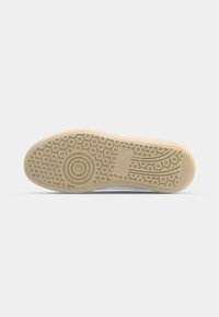 Semelle de chaussure avec semelle extérieure en caoutchouc beige comportant des motifs circulaires et linéaires pour une bonne accroche, sur fond blanc uni.