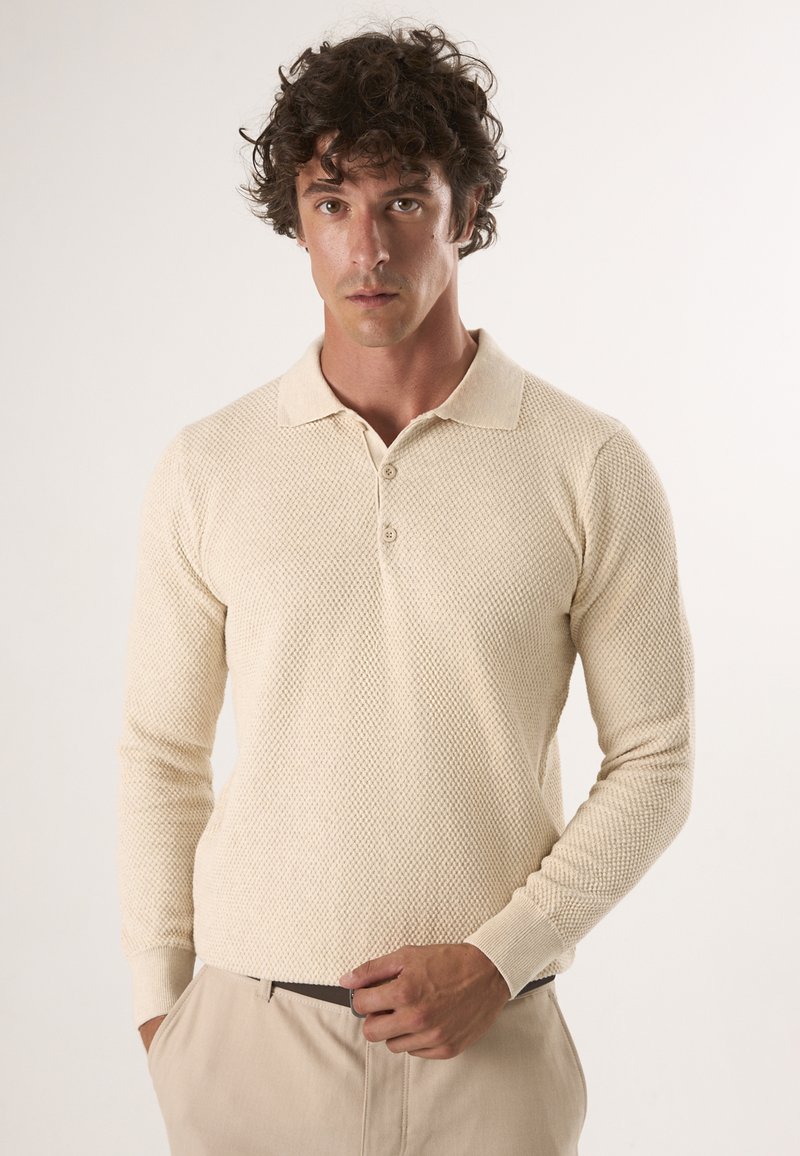 Beige gebreide polo met lange mouwen, voorzien van een textuurpatroon, een klassieke kraag en een drieknoopsluiting. Draag het met beige broeken.