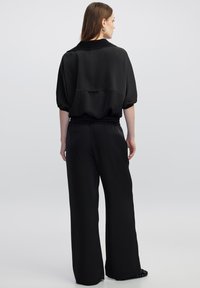 Zwarte pullover met een ontspannen pasvorm en korte mouwen, gecombineerd met brede zwarte broek. Soepele stof met een minimalistisch ontwerp.