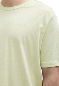 T-shirt à manches courtes vert clair en tissu doux, arborant un logo embossé subtil avec les chiffres "1902" sur la poitrine.