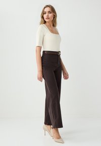 Off-white vierkante hals bodysuit gecombineerd met hoge, donkere bruine broek en beige puntige hakken, met een bruine riem met een gouden gesp.