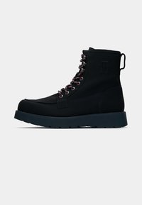 Botas de senderismo negras con una parte superior texturizada, que presentan cordones en rojo y blanco en contraste, una suela gruesa negra y un detalle de logo en relieve en el lado.