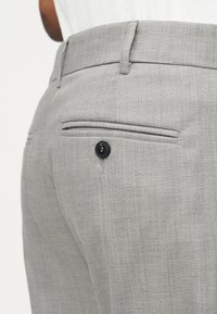 Κοντινό πλάνο ενός ατόμου που φοράει ανοιχτό γκρι παντελόνι φόρεμα με μαύρη πίσω τσέπη με κουμπί και θηλιές ζώνης.