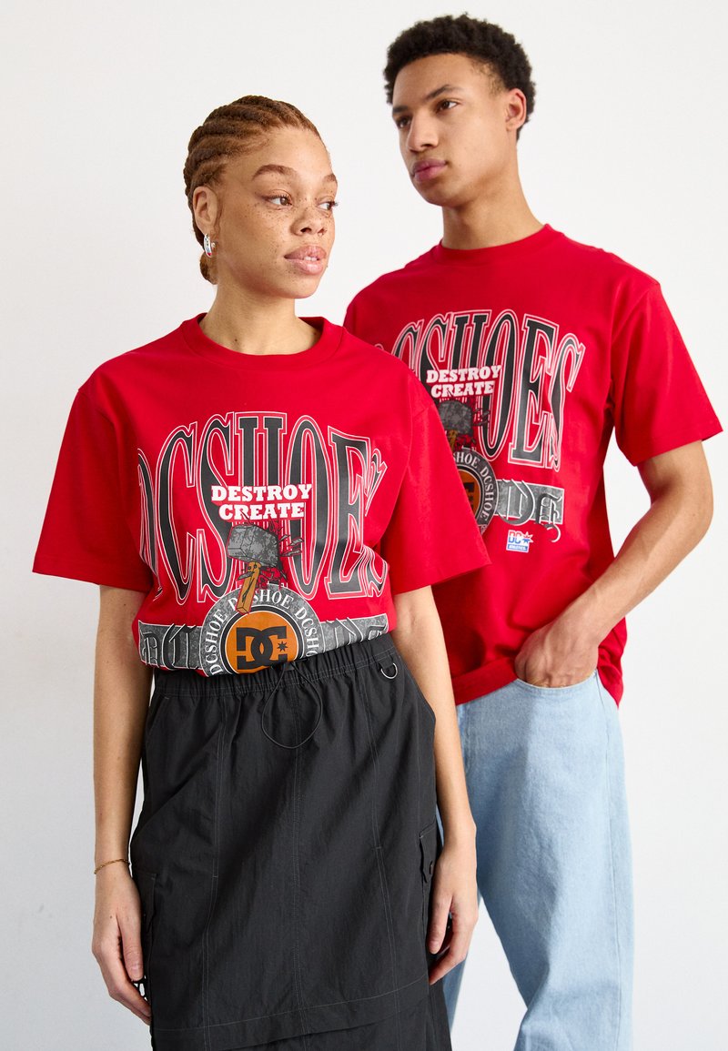 T-shirts graphiques rouges avec des logos et des textes audacieux, associés à une jupe utilitaire noire et à un jean bleu clair, représentant un style décontracté urbain.