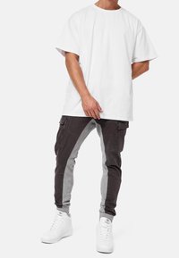 Weißes Baumwoll-T-Shirt mit kurzen Ärmeln, kombiniert mit farblich abgesetzten Jogginghosen in Dunkelgrau und Hellgrau, die über Reißverschlusstaschen und schmal zulaufende Bündchen verfügen.