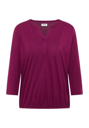 Blouse violette à manches longues avec trois boutons sur un col en V et un ourlet élastique, étiquetée "Cecil" au niveau du col.