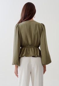 Olive roheline peplum-särk pikkade varrukatega, tekstuurse riidega, elastse vöökoha ja volangäärisega. Tagantvaates on nähtavad varruka detailid.