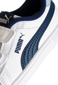 Sneaker White Puma con logo blu navy, striscia laterale testurizzata e chiusura a strappo, che mostra parte della fodera interna della scarpa.