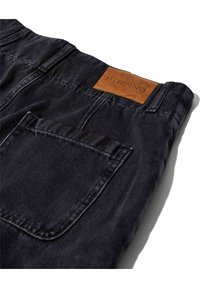 Dunkelblaue Jeans aus Denim mit strukturiertem Finish, ausgestattet mit einem Leder-Label und Details an der Gesäßtasche, im Winkel präsentiert.