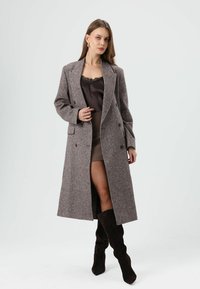 Bruine geruite wollen jas met een dubbelrijig ontwerp, oversized pasvorm en revers met inkeping, gedragen over een donker camisole en rok.