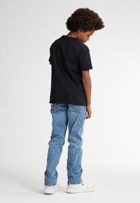 Zwarte katoenen T-shirt, blauwe spijkerbroek, witte sneakers. Zichtbare stiksels en achterzakdetails op de spijkerbroek, platte kraag op het T-shirt.