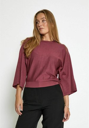 Bordeaux cropped top met brede mouwen en een ronde halslijn, gemaakt van zachte stof. Gecombineerd met zwarte high-waisted broek.