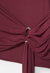 Bordo tkanina skupljena i uvijena kroz mali srebrni metalni prsten, stvarajući naborane nabore i prošiven rub.