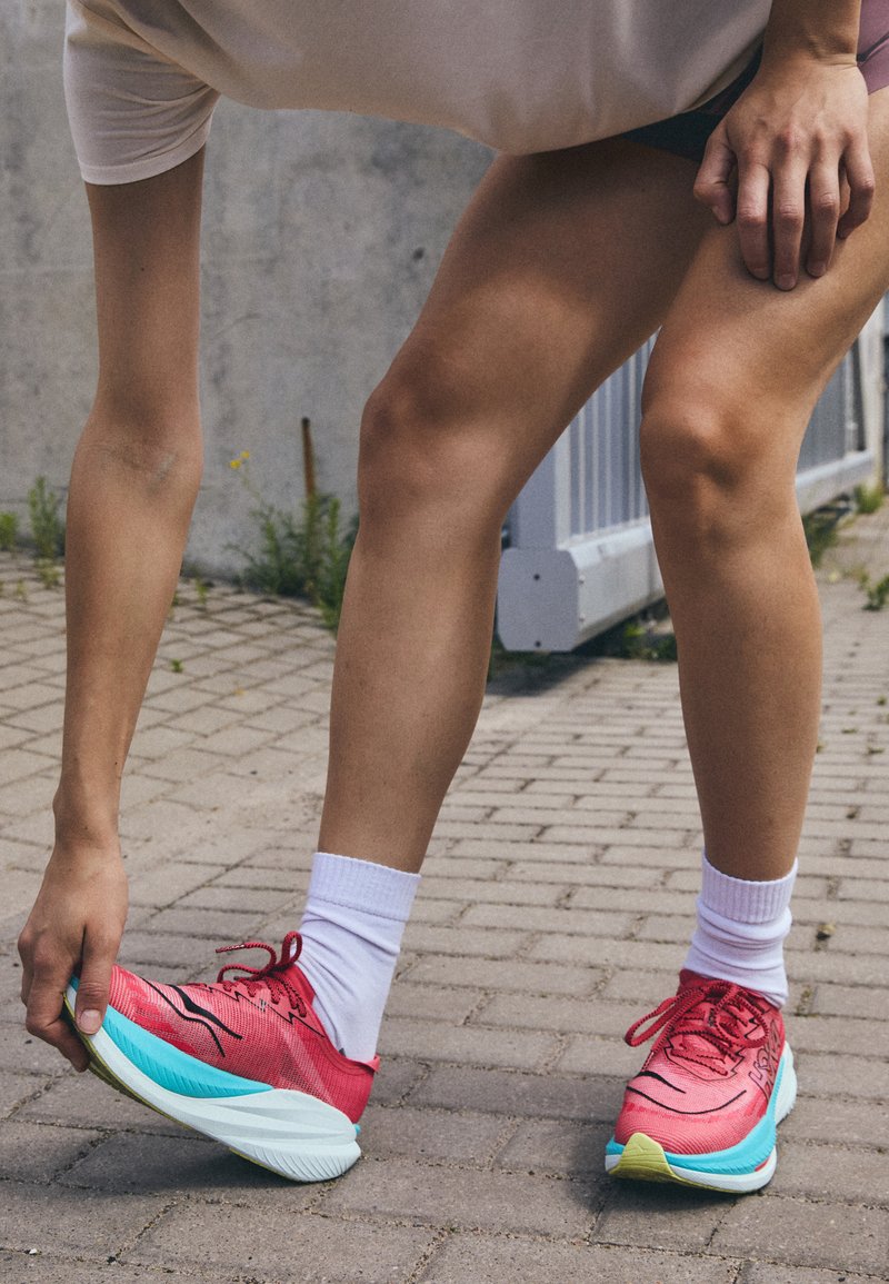 Baskets de sport rouge vif avec une tige en maille, une semelle blanche et aqua, et des accents noirs contrastants. Chaussettes blanches partiellement visibles.