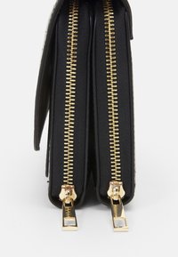 Černá kožená peněženka s dvojitými přihrádkami, zlatými zipy a strukturovaným povrchem. Zipy jsou umístěny na horních okrajích.