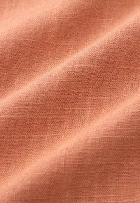 Gros plan sur un tissu tissé doux de couleur pêche avec des fibres texturées visibles et des plis délicats.