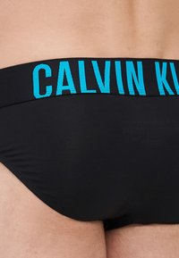 Schwarze Unterhosen mit einem türkisfarbenen "Calvin Klein" Logo-Bund. Glatte Textur, eng anliegende Passform und minimalistisches Design.