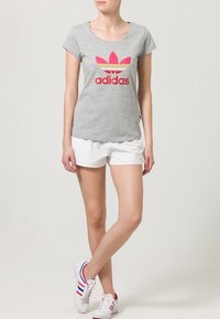 Grå t-shirt med rosa och gula Adidas-logotypen, kort ärm, ihop med vita shorts och avslappnade sneakers i röd, blå och vit.