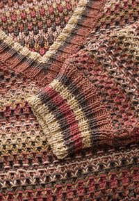 Pulover tricotat cu decolteu în V, textură multicoloră cu dungi în nuanțe pământii de brun, rugină și crem. Cusăturile evidențiate creează un efect mozaicat.