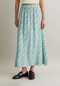 Jupe maxi bleu clair avec un motif floral ; ceinture élastique froncée ; fabriquée en tissu doux ; assortie à des chaussures noires.