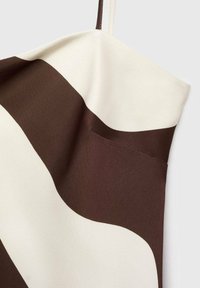 Hnědo-krémová látka s hladkým povrchem a vzorem; obsahuje trojúhelníkový design a malou kapsu integrovánu do látky.