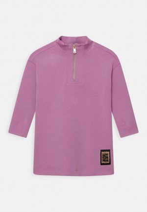 Lilla langærmet pullover med kvart lynlås og lille rektangulær leopardprint-patch nær kanten på hvid baggrund.