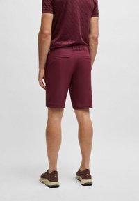 Mörkröda shorts i ett slätt tyg, med skräddarsydd passform, två bakfickor och en ren fåll. Bärs med bruna sneakers.