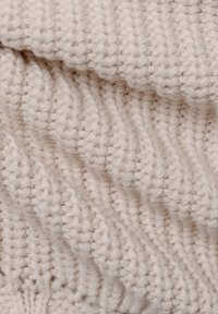 Beige knitted textile featuring a ribbed pattern; soft texture with prominent, rounded stitches creating depth and visual interest.