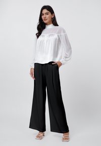 White satin blouse with a high neck and long sleeves, paired with black satin wide-leg trousers. Notable soft texture and drape.