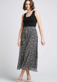 Jupe maxi noire avec des motifs floraux en bleu, jaune et blanc ; matière légère, design fluide, associée à un haut noir ajusté.