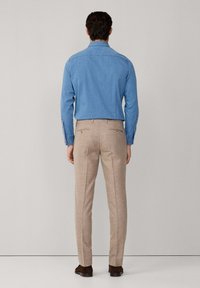 Plava košulja dugih rukava sa dugim rukavima, u kombinaciji s bež krojenim hlačama. Hlače imaju stražnje džepove i glatku teksturu.