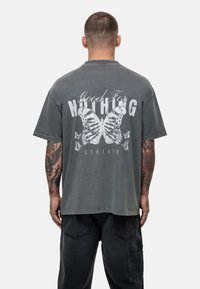 Grijze oversized t-shirt met een vlinderafbeelding en de tekst "Good For Nothing" op de rug. Korte mouwen, ronde hals, casual pasvorm.