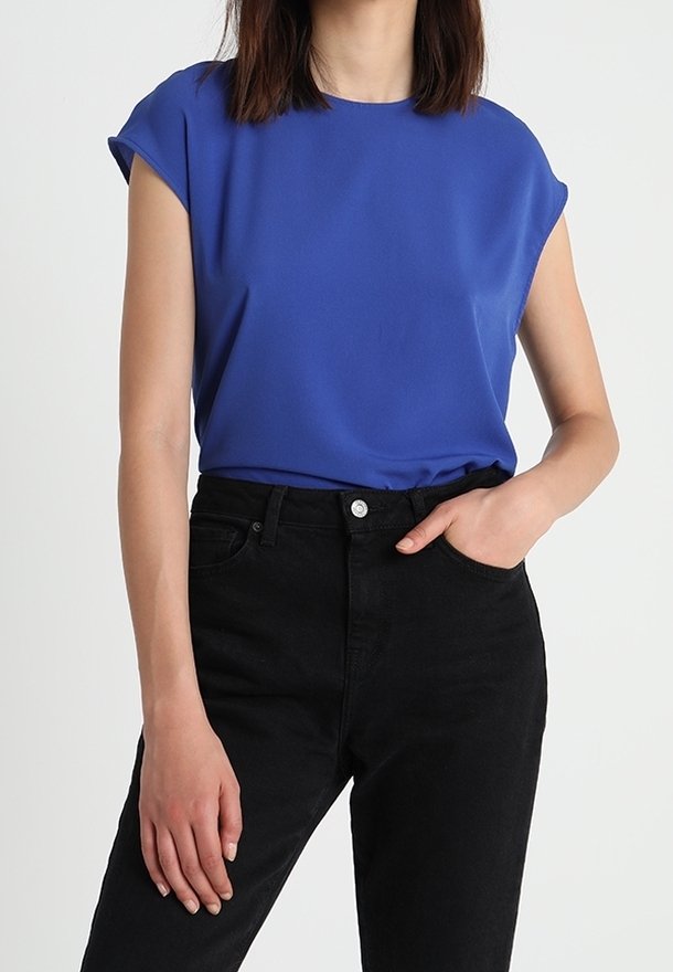 Blauw topje met korte mouwen van gladde stof, gecombineerd met zwarte hooggesloten spijkerbroek. Voorzien van een ronde hals en een ontspannen pasvorm.