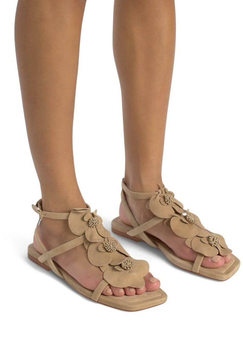 Beige suède sandalen met bloemapplicaties, open teen ontwerp, platte zool en enkelbandje. Kenmerken zijn textuurbladeren en kralenaccenten.