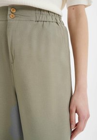 Lichte, olijfgroene broek met een ontspannen pasvorm, voorzien van twee houten knoopaccenten en een elastische tailleband voor comfort.
