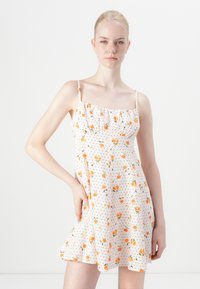 Rochie albă cu modele florale portocalii și verzi, cu buline negre, cu un bust volanat și bretele subțiri ajustabile. Material ușor și design evazat.
