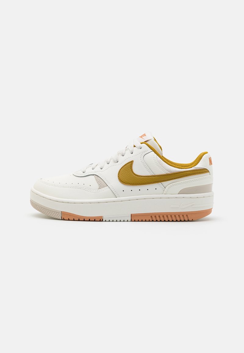 Baskets basses en cuir blanc avec swoosh Nike jaune moutarde, accents et semelle ton pêche sur fond gris clair.