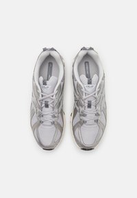 Un par de zapatillas deportivas grises y blancas con cordones, vistas desde arriba sobre un fondo blanco liso.