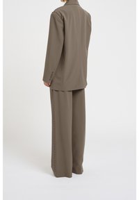 Veste de costume marron et pantalon large assorti, ornés d'accents cloutés le long des épaules et des coutures latérales, avec une texture de tissu lisse.