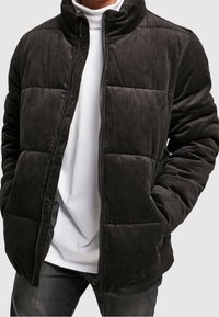 Černá manšestrová prošívaná bunda s vysokým límcem, prošívaným designem a zapínáním na zip. Má texturované pruhy a úzký střih.