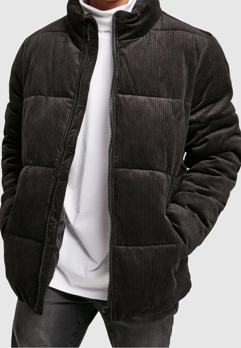 Černá manšestrová prošívaná bunda s vysokým límcem, prošívaným designem a zapínáním na zip. Má texturované pruhy a úzký střih.